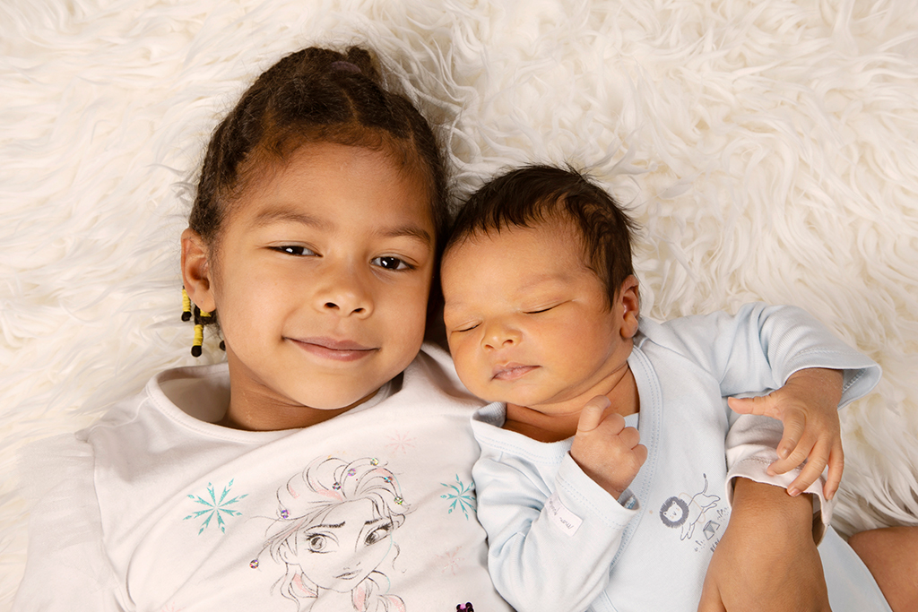 nouveau-né allongé sur un tapis blanc avec sa soeur à ses côtés