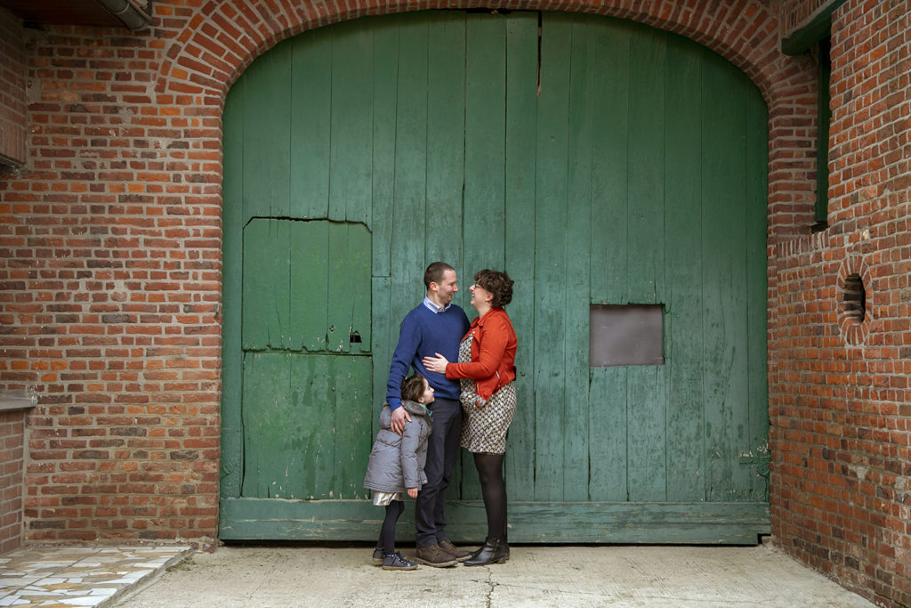 un couple et leur fille qui posent devant une porte en bois verte dans une ferme